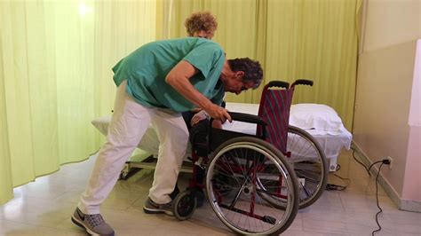 Operatore che assiste un paziente nel passaggio letto-carrozzina