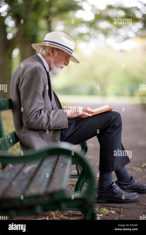 Un anziano sorridente che legge un libro su una panchina in un parco